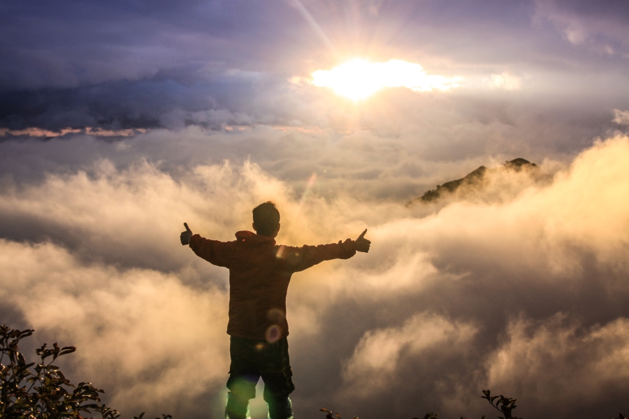 man standing on mountain overlooking clouds
