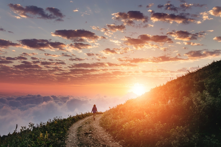 woman walking on curving path on mountain at sunrise